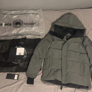 Canada Goose Macmillan - Canada Goose MacMillan Parka – Black Label, grå. Stilren och varm vinterjacka i klassisk design med dunfyllning av hög kvalitet. Kortare modell med justerbar huva, bröst- och sidfickor samt diskret svart Canada Goose-märke på ärmen. Perfekt kombination av funktion och stil för kalla dagar. Storlek: L. Mycket fint skick. Den är lätt använd och säljer den då den inte passar längre.