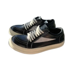 Rick Owens ”Vans” - Snygga svarta sneakers från Rick Owens med vit sula och vita snören. Skorna har en stilren design med kontrasterande vit detalj på sidan och tydliga sömmar. Tillverkade i skinn för en lyxig känsla och passar perfekt till streetwear eller casual outfits.