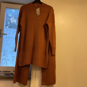 Ny rostbrun stickad set Malle Sportswear - Rostbrun ribbstickad set från Malle Sportswear. Tröjan har lång ärm, rund halsringning och en loose fit. Båda tröjan och byxan har stickat material med snygga vertikala ränder för extra detalj. Perfekt för dig som gillar en chill och trendig look.