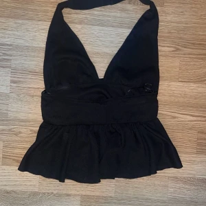 Svart  topp - Säljer en svart halterneck topp med omlott-design och djup v-ringning. Toppen har bred midjedel och volang nedtill som ger en snygg siluett. Perfekt för dig som gillar att sticka ut med en cool och trendig look. För endast 299 priset är diskuterbart