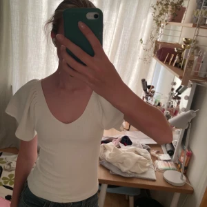 Vit ribbad topp med puffärm från ONLY - Supersöt vit ribbad topp från ONLY i storlek XS. Toppen har v-ringning, puffiga korta ärmar och en snygg öppen rygg med knytband. Materialet är mjukt och stretchigt, perfekt för att ge en slim passform. Perfekt för dig som gillar feminina detaljer och stilren look. Fint skick! 