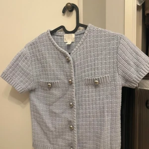 Ljusgrå stickad kofta och kjol H&M XS - Superfin ljusgrå stickad kofta och kjol från H&M i storlek XS. Kortärmad modell med snygga silvriga knappar framtill och på de två dekorativa fickorna. Koftan har en ribbad kant vid ärmslut och halsringning, perfekt för lager-på-lager-stil.