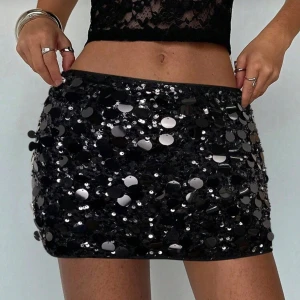 Svart paljettkjol med stora paljetter - Supersnygg svart minikjol täckt med stora, glittrande paljetter som verkligen fångar ljuset. Kjolen har en tight passform och är perfekt för dig som vill sticka ut. Den är kort och har en cool, festlig vibe med massor av attityd.