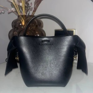 Svart handväska Acne Studios skinn - Snygg svart handväska från Acne Studios i slätt skinn med stilren design och knutdetaljer på sidorna. Jättefint skick bara lite smutsig inuti. finns även en skinnrem/axelrem, skriv för bilder. kom med prisförslag!