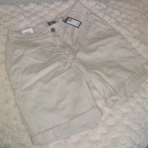 Shorts - Snygga beige shorts från 157, modell Leo, med klassisk design och uppvikta benslut. De har framfickor, bakfickor med knapp och stängs med knapp och dragkedja. Perfekta för varma dagar och har en clean look som funkar till många stilar.