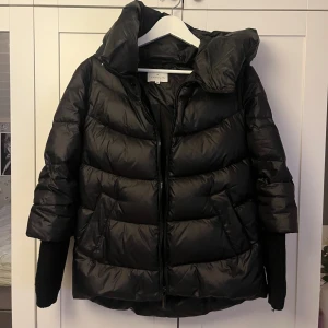 Svart pufferjacka från tatuum  - Säljer en svart pufferjacka från tatuum med hög krage och dragkedja framtill. Jackan har breda, quiltade partier och stickade muddar vid ärmsluten. Perfekt för kalla dagar och har en riktigt snygg oversized look. Storlek 34 men passar även 36