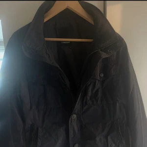 Mörkblå field jacket från J.Lindeberg, storlek M - Snygg mörkblå vindjacka från J.Lindeberg i storlek M. Jackan har hög krage, flera fickor med både dragkedja och knappar samt en stilren look. 