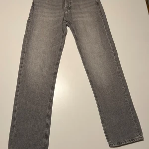 Grå jeans från Jack & Jones Relaxed/Chris - Snygga grå jeans från Jack & Jones, modell Relaxed/Chris. De har en avslappnad passform med raka ben och klassisk femficksdesign. Jeansen är tillverkade i mjukt denim och har en cool tvättad look med svarta detaljer vid knapparna.