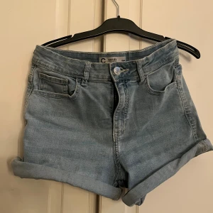 Ljusblå denimshorts från Cubus - Snygga ljusblå denimshorts från Cubus med klassisk femficksdesign och uppvikta benslut. Modellen har normal passform, midwaist och stängs med knapp och dragkedja. Perfekta för varma dagar och chill stil.