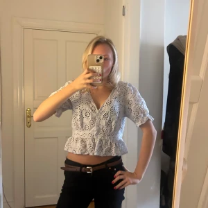 Vit blus med volang och broderi💖💖 - Superfin vit blus med korta puffärmar, v-ringning och broderade hålmönster. Blusen är croppad med volang nedtill och har en feminin, luftig stil som passar perfekt till svarta jeans. Materialet känns som bomull och ger en fräsch vibe.