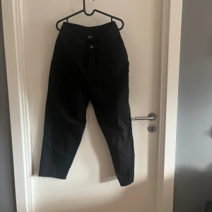 Svarta tapered byxor från 157 - Svarta byxor från 157 i storlek M med tapered passform och croppad längd. Byxorna har knappstängning fram och är tillverkade i ett mjukt bomullsmaterial. 