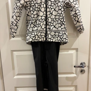 Svartvit regnjacka från, stl 110/116 - Säljer en svartvit regnjacka i storlek 110/116. Jackan har ett unikt mönster med svarta linjer på vit botten, hel dragkedja framtill och elastiska muddar. Materialet är syntet och jackan är perfekt för regniga dagar.