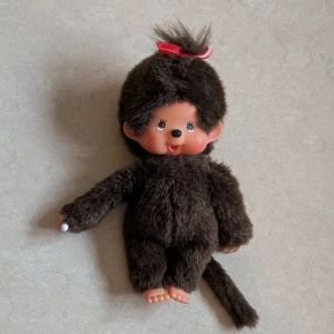 Monchichi - Bilderna visar en Monchichi en mjukisdocka med brun päls, röd rosett och plastdetaljer på händer och fötter. Jätte söt Monchichi 