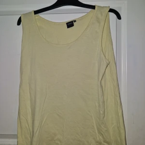 Ljusgul linnetopp från Jonna B - Säljer en enkel och fräsch ljusgul linnetopp från Jonna B. Toppen är ärmlös med rund halsringning och tillverkad i mjuk bomull, perfekt för varma dagar eller som layering-piece. Passar dig som gillar stilrena och bekväma plagg.