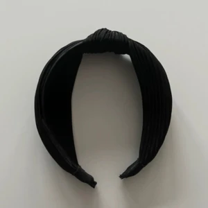 Svart ribbat diadem med knut - Snyggt svart diadem med ribbad struktur och en knutdetalj på toppen. Diademet är brett som ger en stilren och trendig look. Perfekt accessoar för att lyfta vilken outfit som helst.