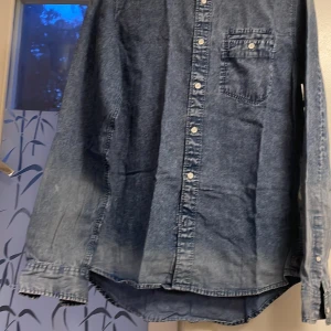 Blå jeansskjorta Calvin Klein Jeans  - Snygg blå jeansskjorta från Calvin Klein Jeans i slim fit. Skjortan har klassisk krage, vit knappstängning och en bröstficka. Perfekt för dig som gillar en chill och stilren vibe. Obs. Varan har små fläckar på armarna.