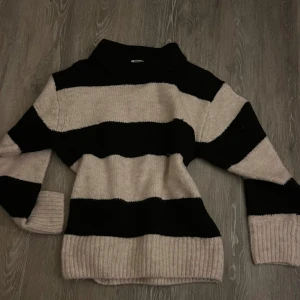 Randig stickad tröja från Gina Tricot - Mysig stickad tröja från Gina Tricot i svart och beige med breda ränder och ribbade muddar. Tröjan passar mig som vanligtvis har xs/s. Perfekt för kyliga dagar och enkel att matcha med jeans eller kjol. Tröjan är aldrig använd bara testad!