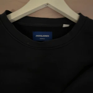 Mörkblå sweatshirt från Jack & Jones - En stilren svart sweatshirt från Jack & Jones med rund halsringning och ribbade muddar vid ärmslut och nederkant. Perfekt för dig som gillar en enkel och klassisk look. Tröjan är i mjuk bomull och har en relaxed passform.