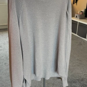 Glittrig silvertröja från Zara - Säljer en snygg långärmad tröja från Zara i storlek S. Tröjan är silverfärgad med glittrigt material som ger en cool och festlig vibe. Den har rund hals och ribbade muddar vid ärmslut och nederkant. Perfekt för dig som gillar att sticka ut. Säljer då den inte kommit till användning 