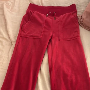 Röda mjukisbyxor Juicy Couture XXS - Snygga röda mjukisbyxor från Juicy Couture i storlek XXS. Byxorna har bred resårmidja med snörning, stora fickor fram och bak med knappar, samt ett broderat Juicy Couture-logo på ena fickan. Mjukt och skönt material som ger en chill vibe.