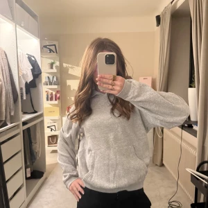 Grå hoodie från H&M med huva - En basic ljusgrå hoodie från H&M med klassisk huva och stor känguruficka framtill. Tröjan har lång ärm och är tillverkad i mjuk bomullsblandning, perfekt för chill dagar. Enkel och stilren design som funkar till det mesta.