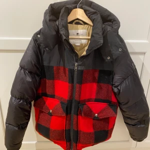 Woolrich Down Jacket  - Säljer en fet pufferjacka från Woolrich i klassiskt röd och svart rutig design. Jackan har huva, stora fickor och dragkedja framtill. Materialmix med dunfyllda partier och ull på rutiga sektioner. Nypris för liknande modeller från Woolrich ligger ofta runt 6 000–10 000 kr. Ett perfekt val för dig som vill ha en unik och snygg vinterjacka som verkligen står ut! Storlek M men passar de som har S också. 