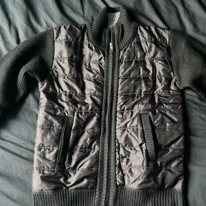 Svart cardigan jacka  - Snygg svart cardigan jacka med quiltad framsida och stickade partier på ärmar, rygg och krage. Jackan har dragkedja framtill och fickor. Storlek M med passar även S lika bra 