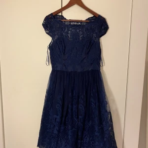 Marinblå spetsklänning från Chi Chi London - Supersnygg marinblå kortklänning från Chi Chi London med spetsdetaljer och genombrutet mönster upptill. Klänningen har en rundad hals, korta ärmar och dragkedja i sidan. Kjolen är lätt utställd och har ett elegant broderat mönster. Perfekt för dig som vill sticka ut!