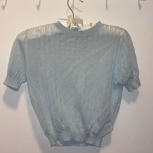 Ljusblå topp från Zara - Supersöt ljusblå topp från Zara med korta ärmar och diskret hålmönster. Tröjan har ribbade muddar vid ärmslut och midja. Storlek xs