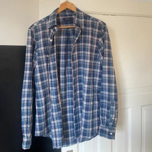 Blårutig skjorta från Polo Ralph Lauren - Snygg blårutig skjorta från Polo Ralph Lauren med klassisk krage och knappar framtill. Skjortan har långa ärmar och är gjord i mjuk bomull. Jag har köpt skjortan på secondhand men aldrig använt då den är lite för stor för mig. Skjortan är i mycket bra skick.