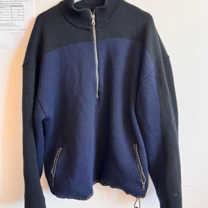 Marinblå half zip tröja från Ivanhoe - Snygg marinblå och svart stickad tröja från Ivanhoe i 100% merinoull. Tröjan har hög krage, half zip-dragkedja och två dragkedjefickor framtill. Perfekt för kyliga dagar och riktigt skön att ha på sig.den har även windstopper
