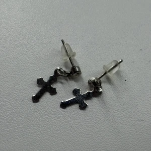 Silvriga korsörhängen med sten - Ett par stilrena örhängen i silverfärg med hängande kors och en liten glittrande sten vid fästet. Perfekta för dig som gillar klassiska detaljer med en modern twist. Säljs som par.