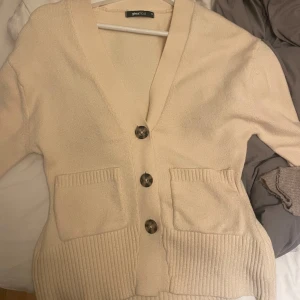 ljusgul kofta från Gina Tricot XS - Säljer en ljusgul kofta från Gina Tricot i storlek XS. Koftan har ribbade muddar, två fickor framtill och stora knappar. Den är stickad och har en djup v-ringning som ger en chill vibe. Perfekt att slänga på sig när det är lite kyligt ute.