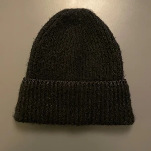 Svart ribbstickad mössa från H&M - En svart ribbstickad mössa från H&M i onesize. Klassisk modell med uppvikt kant och mjukt, värmande material. Den har en glittrig kant upptill 💕Perfekt för kalla dagar och enkel att matcha med alla outfits.
