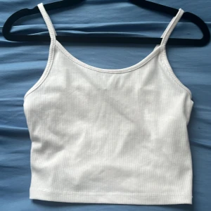 Vit  linnetopp - Säljer en fräsch vit linnetopp från Sister i storlek M. Toppen har smala axelband och är ribbad för en snygg och enkel look. Perfekt att styla med jeans eller shorts. Materialet är mjukt och stretchigt, vilket gör den skön att bära hela dagen.