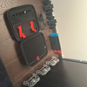 Nintendo Switch med tillbehör och Mario Kart 8 Deluxe - Nintendo Switch i fint skick med original Joy-Con, dockningsstation, tre extra genomskinliga handkontroller, laddare, bärväska och spelet Mario Kart 8 Deluxe. Perfekt för spelkvällar med vänner. Allt fungerar och är redo att användas direkt.