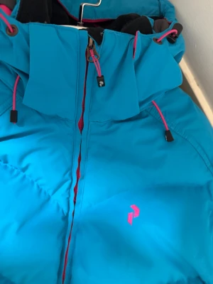 Blå dunjacka Peak Performance - skidjacka - Säljer en blå dunjacka från Peak Performance i storlek L. Jackan har huva med rosa snören, dragkedja framtill och diskret logga på bröstet. Insidan är fodrad i rosa och jackan har flera praktiska fickor. Perfekt för kalla dagar när du vill hålla värmen. Ordinarie pris ca 2500