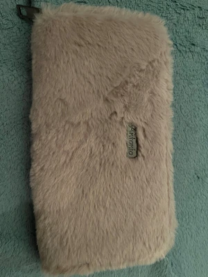 Ljus lila fluffig plånbok från Antonio - Säljer en ljus lila fluffig plånbok från Antonio med pälsliknande material på utsidan och dragkedja runtom. Insidan har flera kortfack och ett myntfack med dragkedja. Perfekt för dig som vill ha en unik och mysig accessoar i väskan.