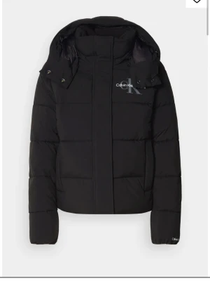 Svart pufferjacka från Calvin Klein Jeans - Säljer en svart pufferjacka från Calvin Klein Jeans med stor huva och logga på bröstet. Jackan är helt ny med prislappen kvar på.