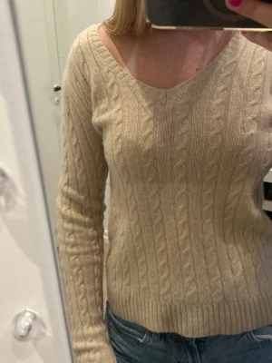 Beige kashmirtröja Ralph Lauren - Kashmir tröja från Ralph Lauren. V-ringad modell med ribbade muddar och diskret RL-brodyr på bröstet. Perfekt till jeans för en clean och klassisk look.