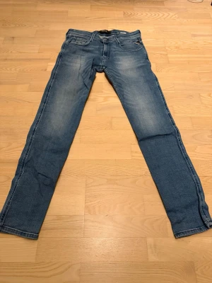 Replay Anbass  - Säljer ett par Replay Anbass jeans i klassisk blå tvätt. De har en slim passform med raka ben och snygga slitningar framtill och baktill. Jeansen har fem fickor, knappgylf och Replay-logga på knappen. Perfekta till sneakers eller boots.