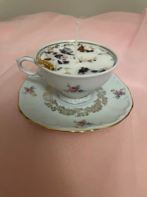 Doftljus i en vit tekopp med blommor i doft utav vanilj nr 1  - Det här ljuset är gjort av återanvändbara material. Tekoppen är köpt secondhand och stearinet är från kyrkor som tänkte slänga det. Det här ljuset har en svag doft utav vanilj, så känsliga även kan använda det. Det här ljuset har även torkade blommor och torkad apelsin på som dekoration. Det finns fler av denna design på hemsidan om man vill köpa sets. 