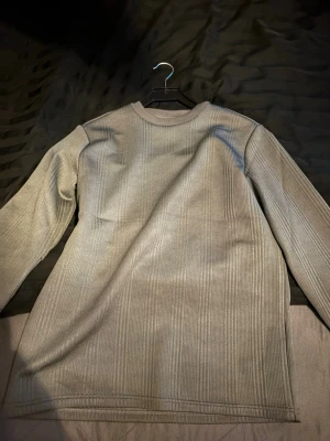 Beige ribbad långärmad tröja - Säljer en beige långärmad tröja med ribbad struktur. Tröjan har en enkel, rak passform och rund halsringning. Perfekt för lager på lager och funkar till många olika stilar.