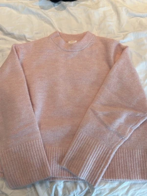 Ljusrosa stickad tröja - Mysig ljusrosa stickad tröja med rund hals och breda ribbade muddar vid ärmslut och nederkant. Perfekt för kyliga dagar och enkel att matcha med jeans eller kjol.