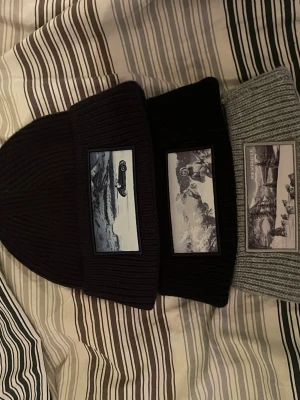Tre svarta stickade revenite mössor - Tja säljer tre stickade mössor från Revenite med ett stort fototryck framtill som visar ett retro bilmotiv i svartvitt. har en grov ribbad struktur och är gjord i ett mjukt material som känns skönt mot huvudet. Perfekt för dig som gillar unika detaljer och streetstyle. Dom sitter perfekt på huvudet och är otroligt sköna. Dom är perfekta nu inför vintern. Hör av dig om du har frågor. (Står att färgen är svart men en är svart och en mörkblå och en grå) kom med pris förslag för alla tre mössor