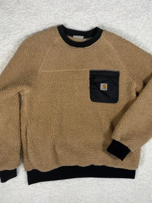 Beige fleece tröja Carhartt WIP - Säljer en beige fleece tröja från Carhartt WIP i storlek S. Tröjan har svart bröstficka med dragkedja och Carhartt-logga, svarta muddar och krage. Perfekt för kalla dagar och riktigt skön att ha på sig. Nypris: 1500!