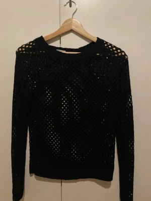 Svart stickad nättröja - Säljer en svart stickad nättröja med lång ärm. Tröjan har ett coolt genombrutet mönster som ger en edgy vibe och passar perfekt över ett linne eller t-shirt. Enkel rund halsringning och mjukt material.
