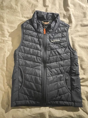 Mörkblå dunväst från Didriksons - Säljer en mörkblå dunväst från Didriksons. Västen har två fickor och en orange detalj på dragkedjan. Perfekt för lager-på-lager och snygg till både jeans och hoodie. Storlek 140 