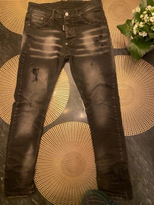 Svarta skinny jeans från Dsquared2 - Säljer ett par svarta skinny jeans från Dsquared2 i storlek 46. Jeansen har slitna detaljer och diskreta hål för en edgy look. Klassisk femficksmodell med knappgylf och snygga slitningar framtill. Perfekta för dig som gillar streetstyle.