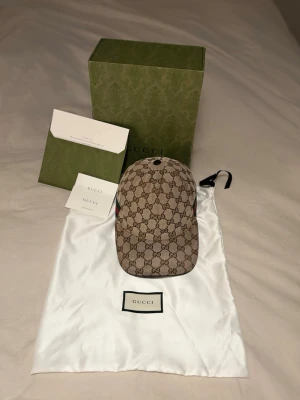 GG Keps - Säljer en beige keps med det klassiska mönstret över hela kepsen och gröna/röda detaljer på sidan. Justerbar rem bak i svart läder och insida med äkthets bevis och kvitto kommer till Kommer med originalpåse, box och certifikat. Storlek S in princip helt ny.